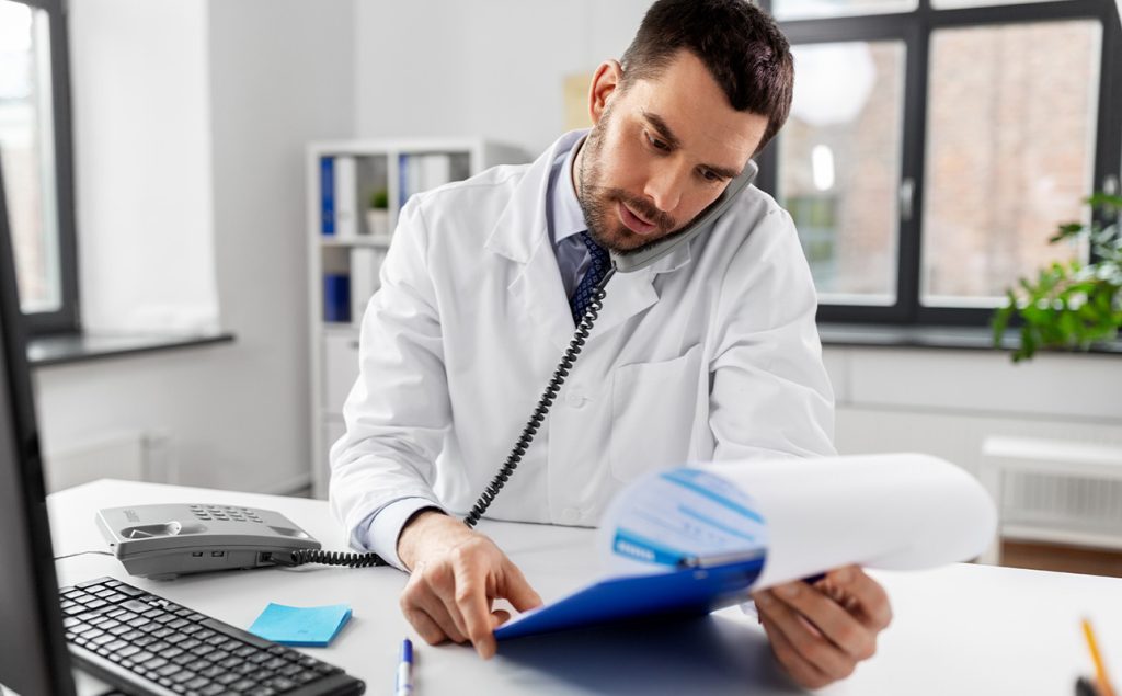 Médico revisando planilhas contábeis com atenção aos impostos.